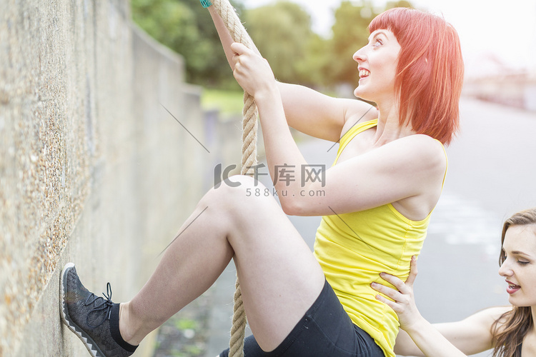 年轻女子用绳子爬过墙