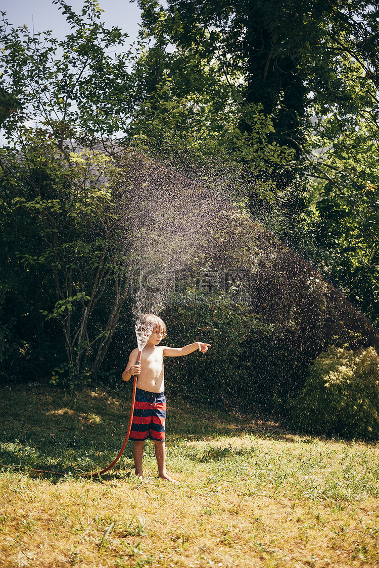 全景男孩在花园里拿着喷水软管看