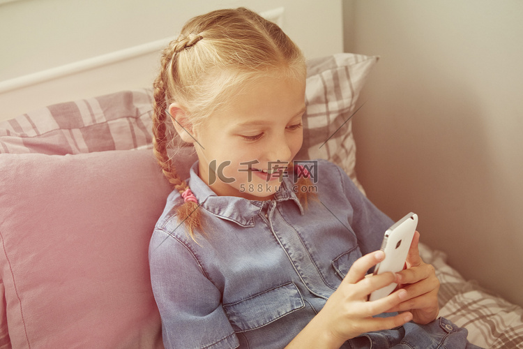 女孩坐在床上低头看智能手机微笑