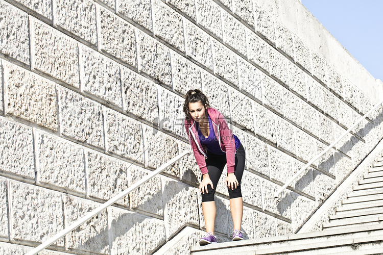 年轻女跑步者在城市楼梯上休息