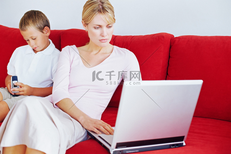 母子俩使用笔记本电脑和手机