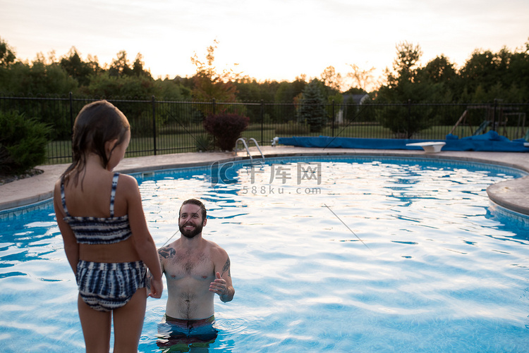 小女孩站在游泳池边泳池里的父亲