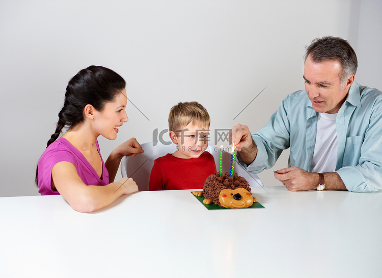 为儿子在蛋糕上点蜡烛的夫妇