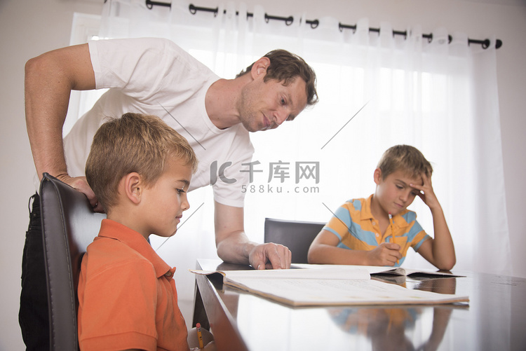 一名男子在餐桌上给两个儿子辅导