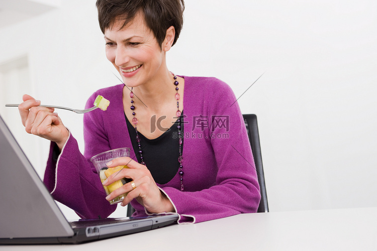 一名妇女在她的电脑前吃饭