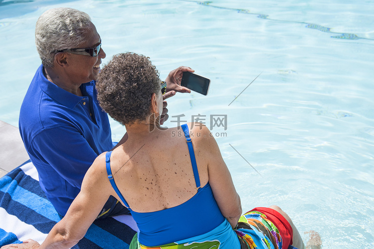 一对老年夫妇坐在游泳池边用智能