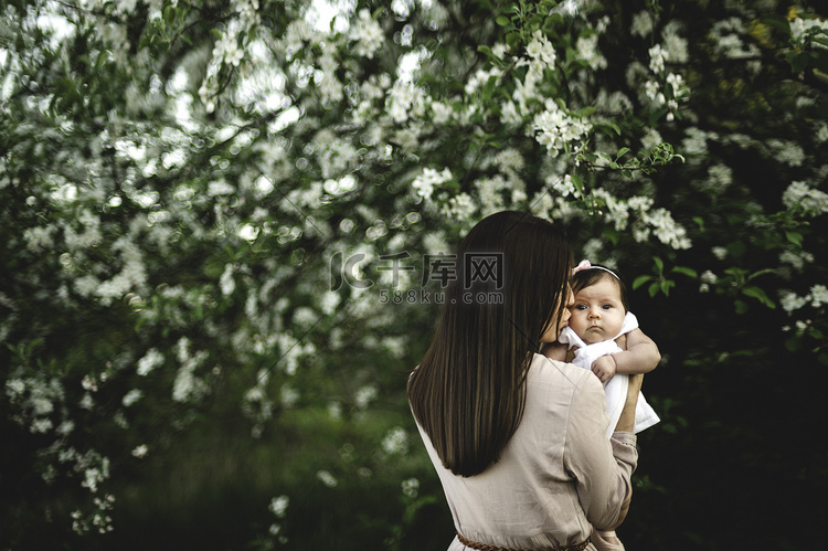 妇女在花园苹果花旁亲吻小女儿的