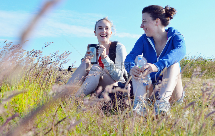 两个年轻女子坐在草地上边喝边聊