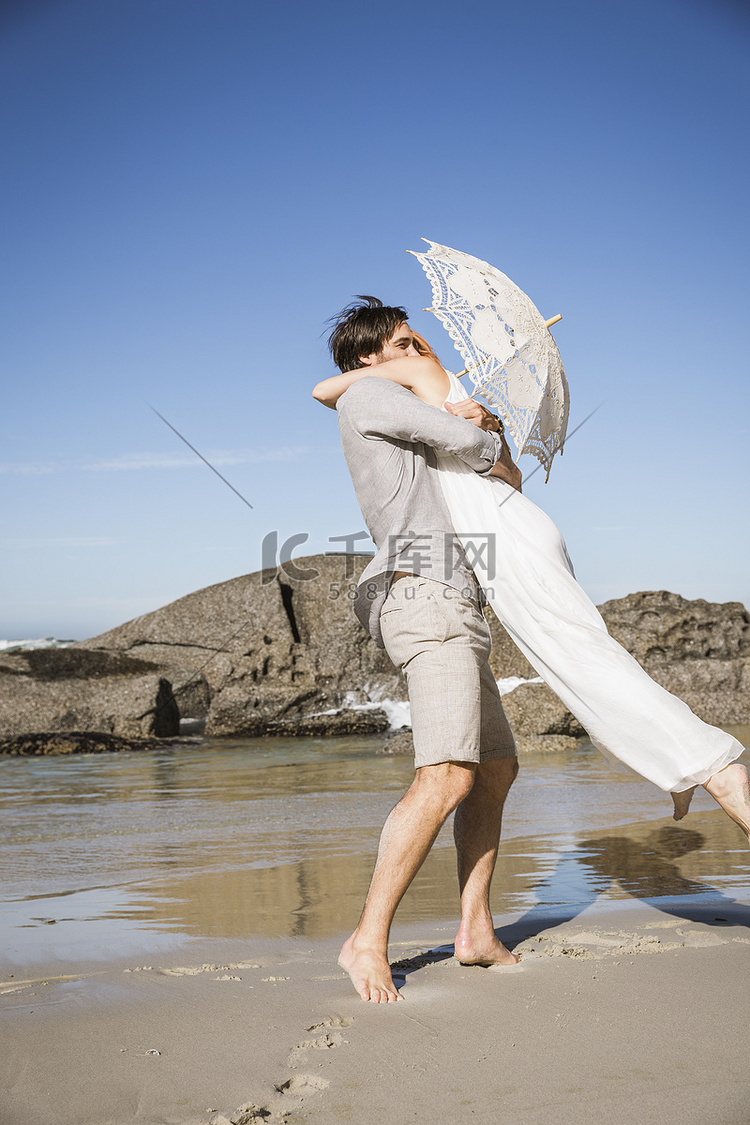 海滩上的情侣抱着蕾丝雨伞侧观