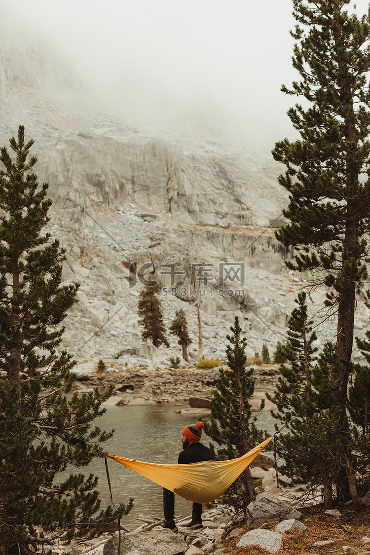 男性徒步旅行者坐在湖边吊床上的