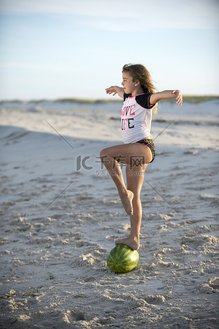 海滩上的年轻女孩在西瓜上保持平