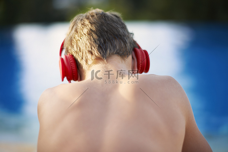 泳池边戴着耳机的十几岁男孩的后