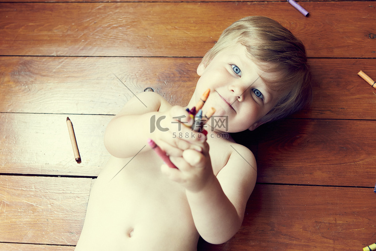 男孩仰卧在木地板上手里拿着蜡笔