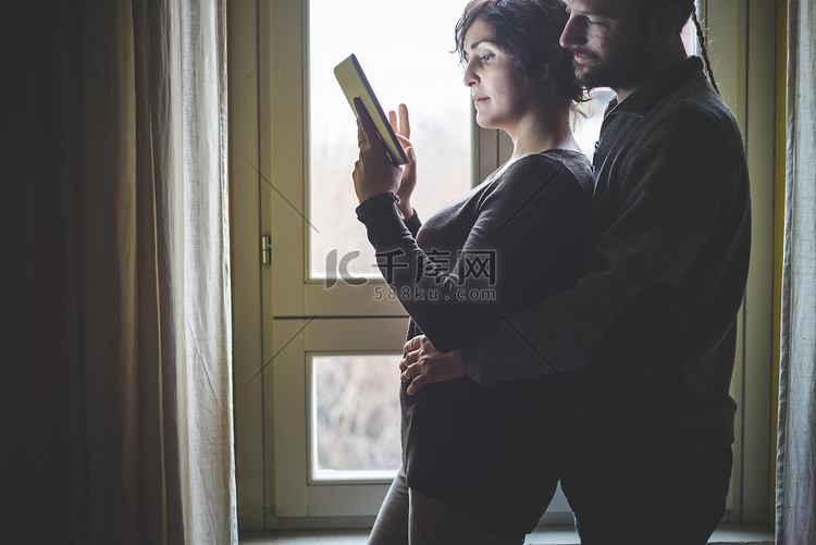 一对夫妇站在窗边用着数字平板电