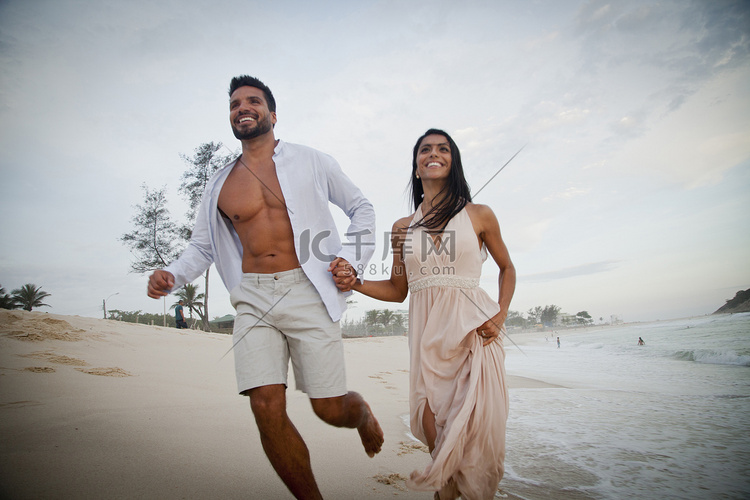 中年夫妇沿着海滩奔跑手牵手低角