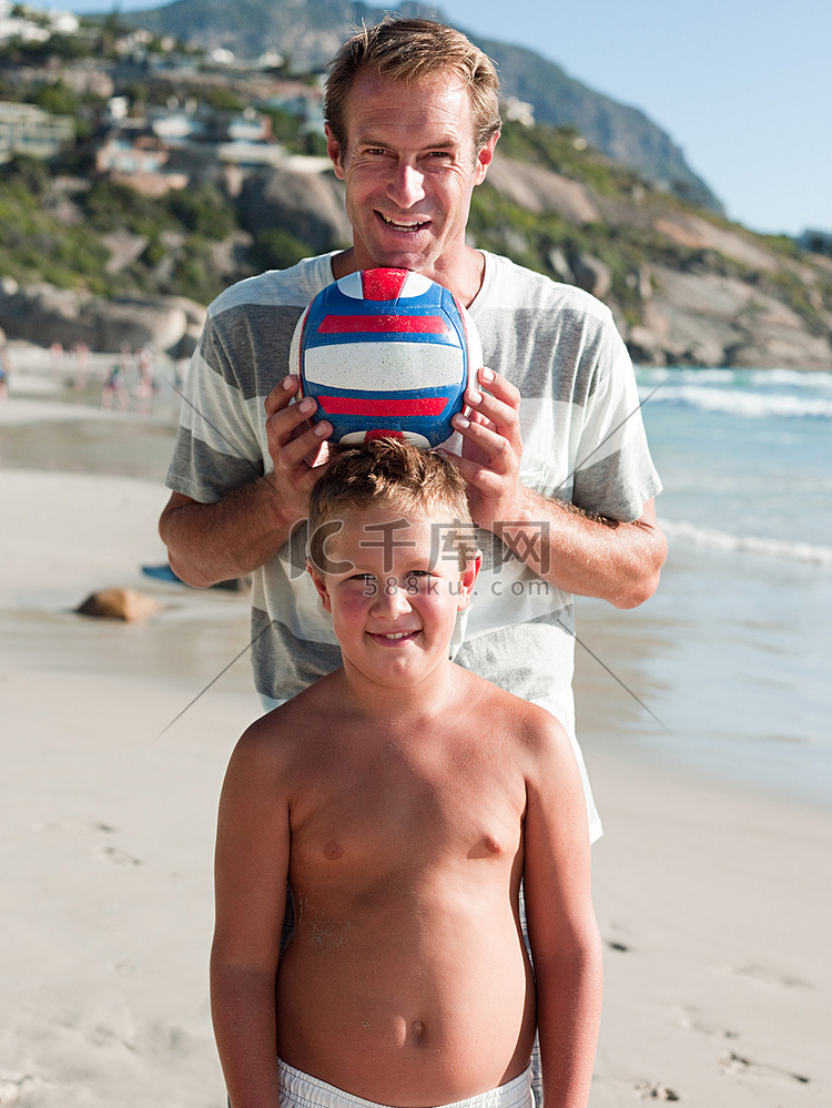 带着球在海滩上的父子