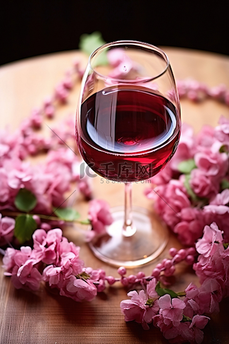 木桌上的一杯红酒和粉红色的花朵