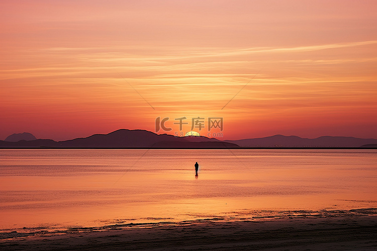 一个人站在日落时的海滩上