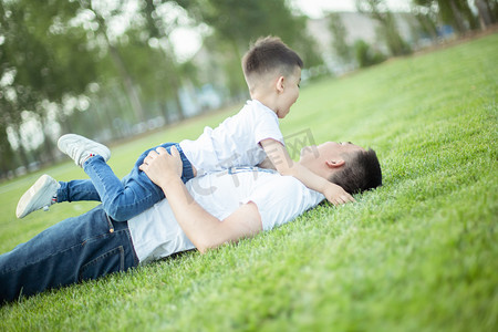 家庭和谐摄影照片_躺在草坪上玩耍的父子俩