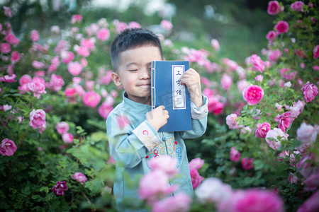 人像小孩摄影照片_站在花丛里用三字经挡脸的小男孩