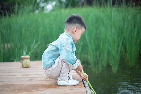 蹲在栈桥上捞鱼的小男孩