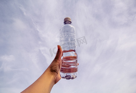 透明清新摄影照片_天空背景下手里拿着一瓶水摄影图