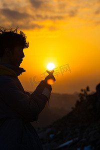 太阳图摄影照片_夕阳下对着太阳比心男孩摄影图