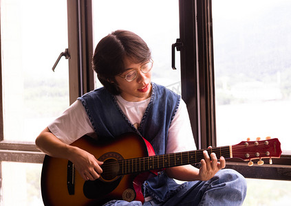 吉他社团摄影照片_坐在窗边弹吉他的男生