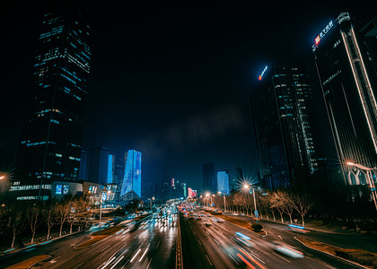 灯光下的城市夜景摄影照片_城市夜景高楼大厦下道路上行驶的车辆
