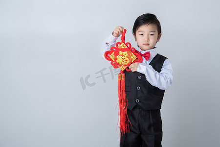 拜年拜年摄影照片_新年新春拜年穿西服的男童室内单背景拿着中国结摄影图配图