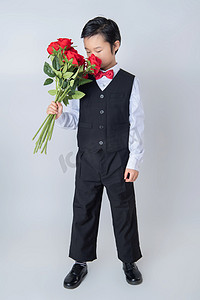 情人节白天穿西装的帅气儿童室内单背景手拿玫瑰花摄影图配图