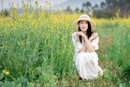金黄色田野摄影照片_白天户外田地的油菜花海中穿着白裙的少女摄影图配图