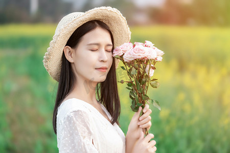 白天户外油菜花海中闭着眼手捧鲜花的少女摄影图配图