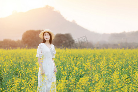 春景人像摄影照片_户外日落时油菜花海中的白衣微笑少女摄影图配图