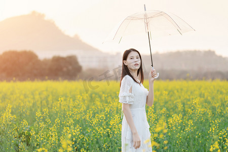 春景摄影照片_户外阳光下油菜花海中手撑着伞的少女摄影图配图