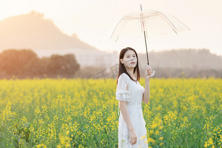 春天田野阳光摄影照片_户外阳光下油菜花海中手撑着伞的少女摄影图配图