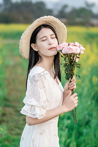 金黄色田野摄影照片_白天户外油菜花海里手捧鲜花的少女摄影图配图