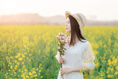 春景摄影照片_阳光下的油菜花海中白衣少女闭着眼手捧鲜花摄影图配图