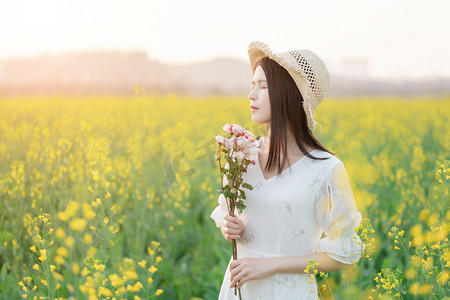 阳光下的油菜花海中白衣少女闭着眼手捧鲜花摄影图配图