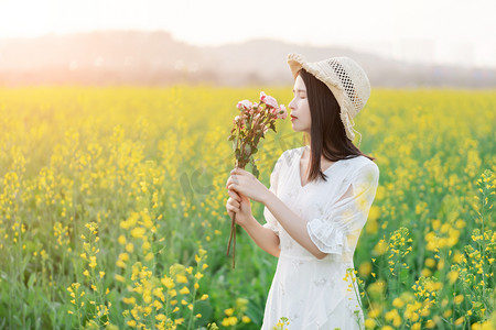 春景摄影照片_阳光下的油菜花海中少女手捧鲜花闻花香摄影图配图