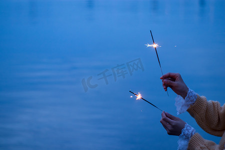 海边夜晚摄影照片_烟花棒晚上火花海边庆祝摄影图配图