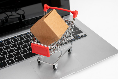 电子购物棚拍笔记本电脑上的购物车货物网购概念静物摄影图配图
