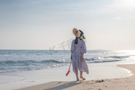 海边带帽子的女人下午穿碎花衣服的女人沙滩散步摄影图配图
