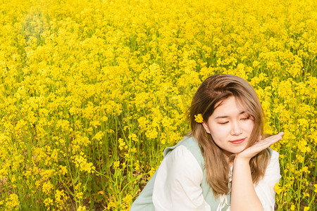 油菜花少女白天油菜花少女油菜花田头戴黄花摄影图配图