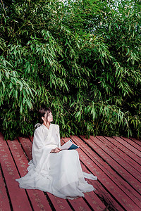 竹叶古风摄影照片_古风美女竹林旁坐地板上读书摄影图