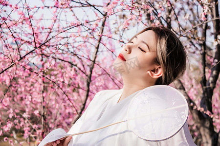 桃花古风摄影照片_古风美桃花园手拿园扇陶醉摄影图