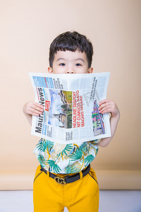 儿童观影照片摄影照片_儿童男孩男童白天小男孩室内影棚拿着报纸躲猫猫摄影图配图