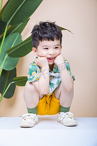 时尚创意杂志摄影照片_儿童童趣白天可爱小男孩室内托着脸大笑摄影图配图