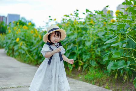 花海女孩摄影照片_儿童孩子向日葵小女孩下午女童2岁儿童花海吃糖奔跑正面摄影图配图