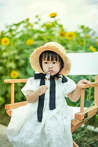 儿童孩子草帽女孩棒棒糖下午小女孩向日葵花海正面吃糖摄影图配图
